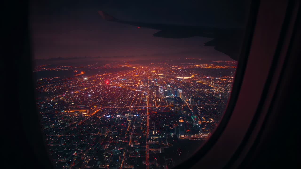 Gliding plane over illuminated city grid at night through window frame, wing silhouette edging view