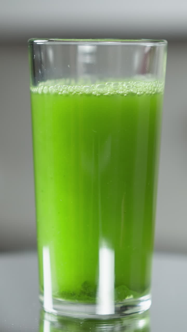 un vaso lleno de jugo verde vibrante con luz natural y espuma delicada en la parte superior