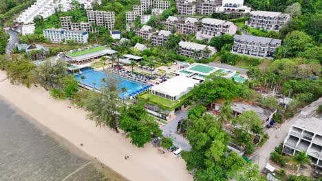 aerial footage showcasing a luxury resort in phuket, thailand, highlighting lush greenery, beachfront, and modern architecture under bright daylight