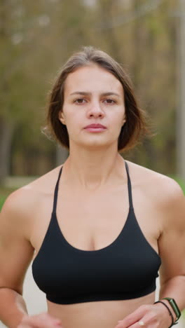 close-up of athletic woman in black sportswear running through park, with blurred background featuring concrete bench, poles, trees, and iron fence, ideal for fitness, jogging, and outdoor activities