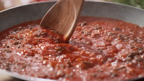 stirring tomato sauce with minced meat using an olive wood spoon - skillet filled with thick bubbling sauce for spaghetti bolognese, dolly out