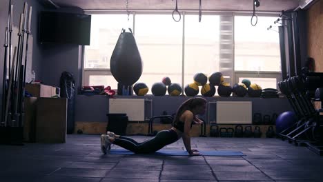 Footage-of-a-sportive-brunette-girl-working-out-at-the-gym,-jumping-into-plank-on-floor-mat.-Fitness-and-healthcare.