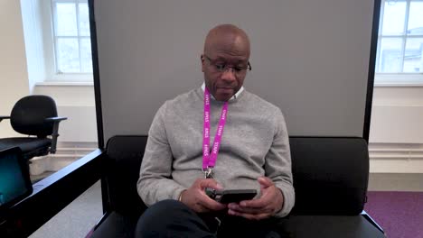 employee engaged in browsing the internet on a smartphone while seated in a quiet, soundproof office pod, promoting focus and productivity