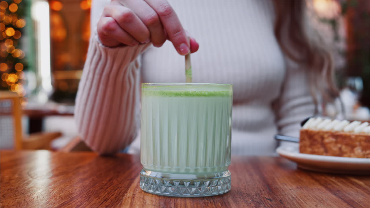 Close up of a woman mixing a matcha latte with a paper straw at a cafe