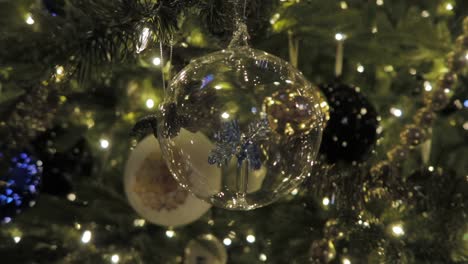 Beautiful-christmas-decoration-made-of-glass-hanging-in-a-christmas-tree-full-of-lights,-close-up-shot