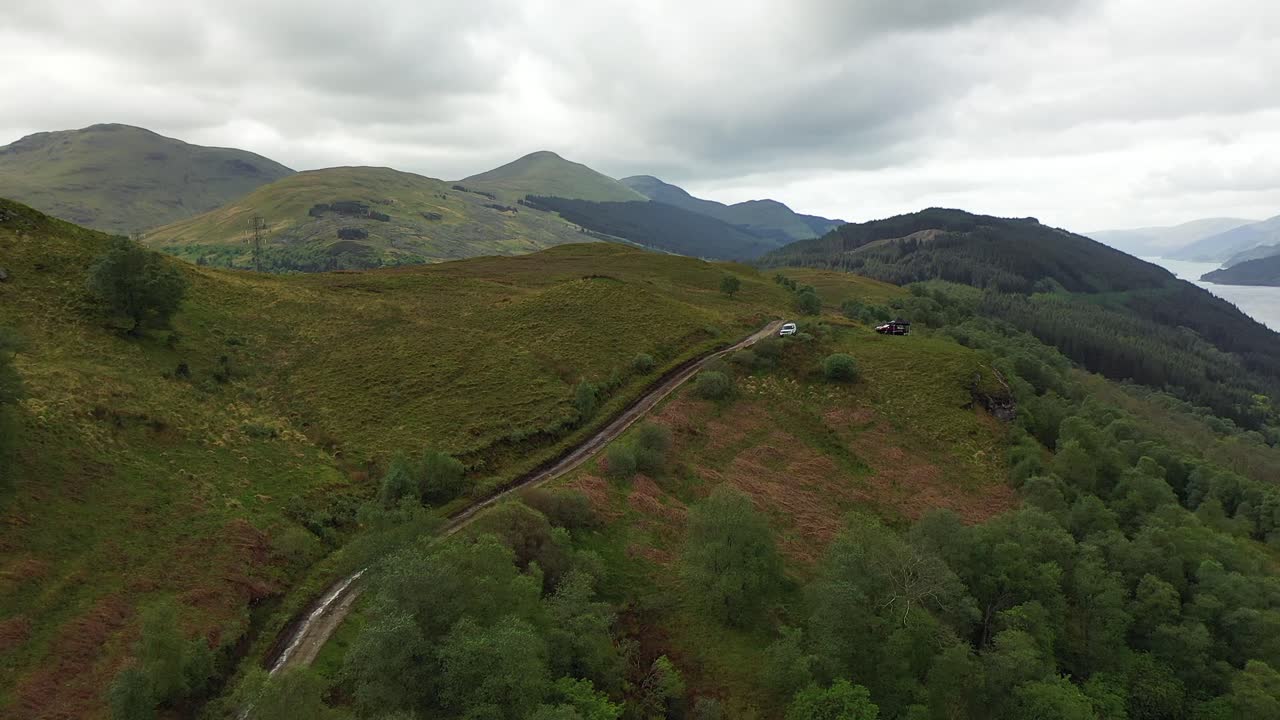 Green mountain aerial in Scottish highlands, drone shot of picturesque valley with dirt track and loch below, Scotland.