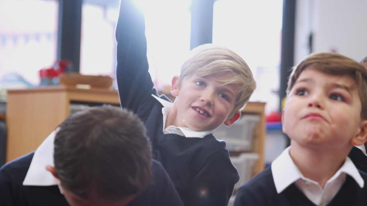 네 명의 초등학교 아이들이 수업에 앉아서 듣고, 한 명이 손을 들고 대답하고, 가까이 가서, 백라이트하고