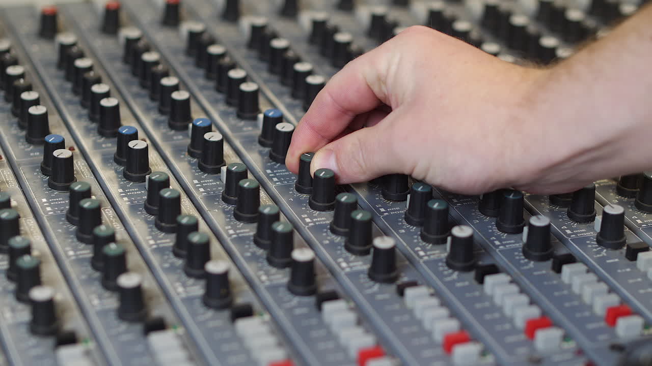 A sound engineer music producer in recording studio adjusting the audio on a grey mixing desk turning the knobs and pressing buttons