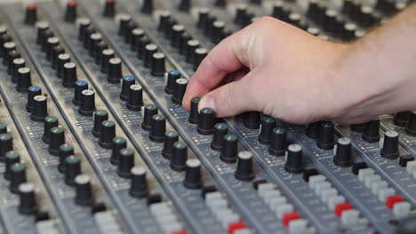 un productor de música ingeniero de sonido en un estudio de grabación ajustando el audio en una mesa de mezclas gris girando las perillas y presionando los botones