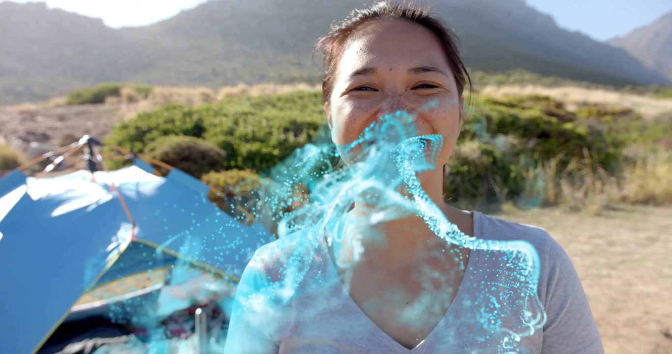 Woman smiling at campsite emitting tech particles from chest forming holographic mask for tech demo