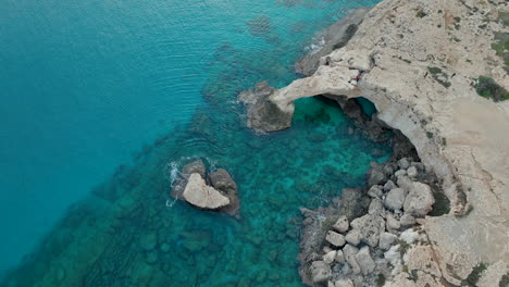 puente del amor - de arriba hacia abajo dramático arco marino a lo largo de la costa de ayia napa con aguas cristalinas azules y rocas sumergidas visibles debajo de la superficie, mar mediterráneo claro y costa accidentada