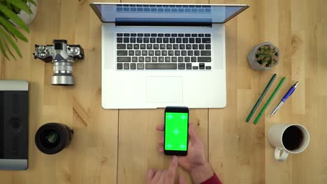 hombre usando el teléfono con pantalla verde, trabajando en la mesa plana