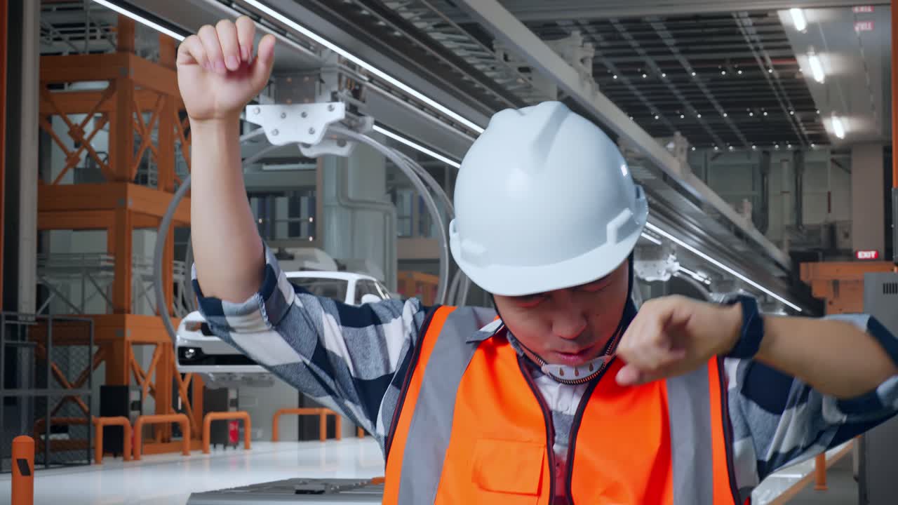 Close Up Of Asian Male Engineer With Safety Helmet Screaming Goal And Dancing Celebrating In EV Car Factory