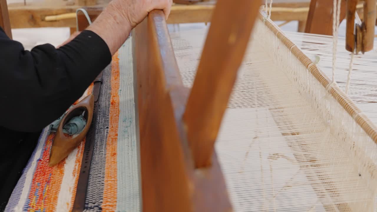 usando un telar tradicional para tejer, una mujer avanza para colocar la lana en su lugar.