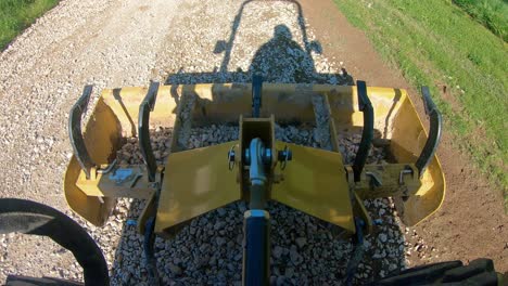 Box scrapper leveling on a new graveled driveway, shadow of tractor and operator are visible