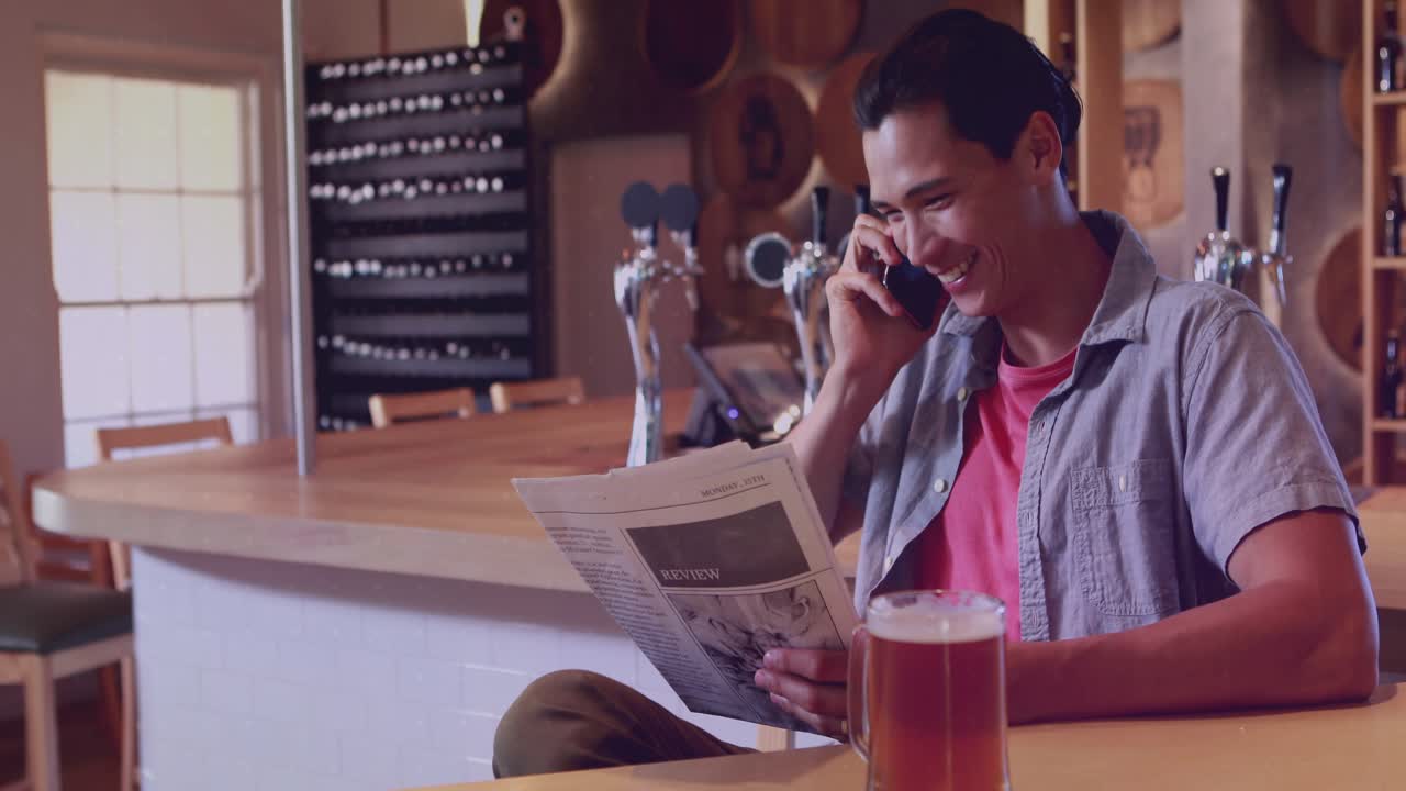Man at bar glancing then lifting phone, sharing article while charts obscuring paper and pint