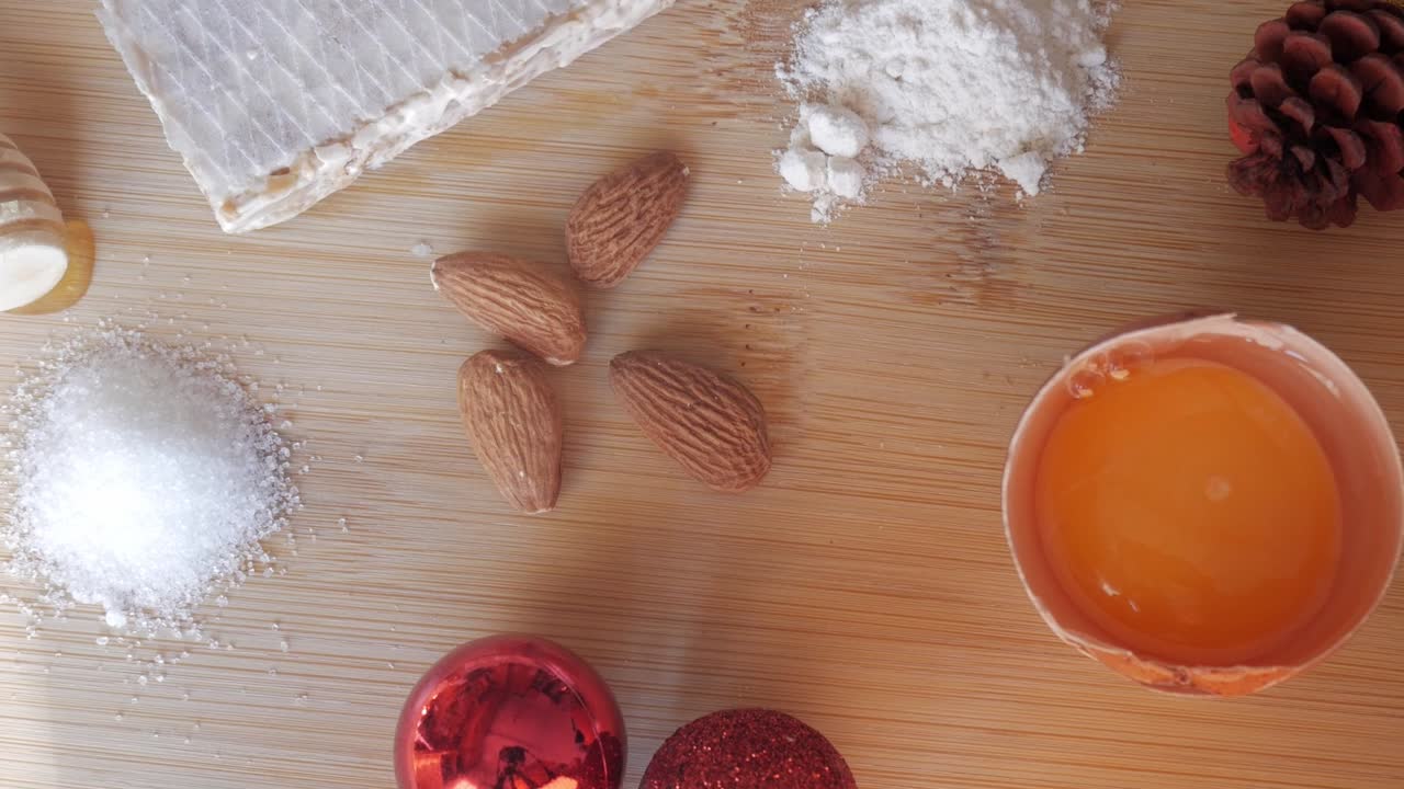 Top-down close-up of ingredients for Pan de Cádiz including almonds, egg yolk, sugar, and flour on a wooden surface under warm light