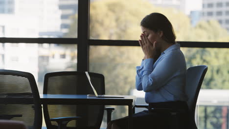 stressed or tired mature businesswoman working on laptop sitting at boardroom table