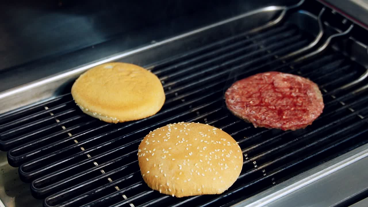 Chef frying buns and cutlet on grill. Cooking meat for hamburger. Cook's hand checking bun while frying on hot grill. Junk food