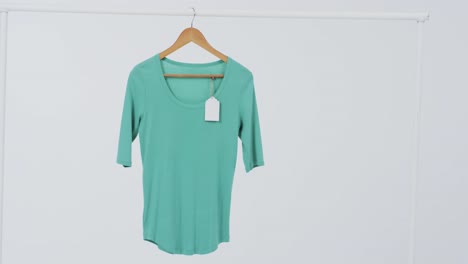 video of green t shirt with tag on hanger and copy space on white background