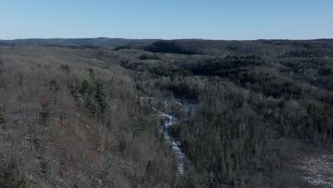 Frozen-Stream-Flowing-Between-Dense-Trees-In-The-Mountains-Of-Quebec,-Canada-During-Winter