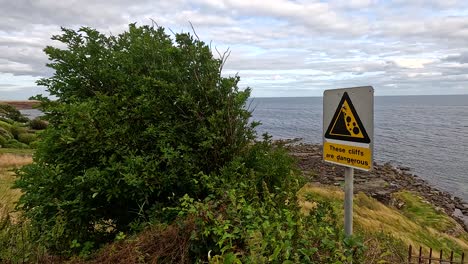 sign warns of dangerous cliffs by the sea