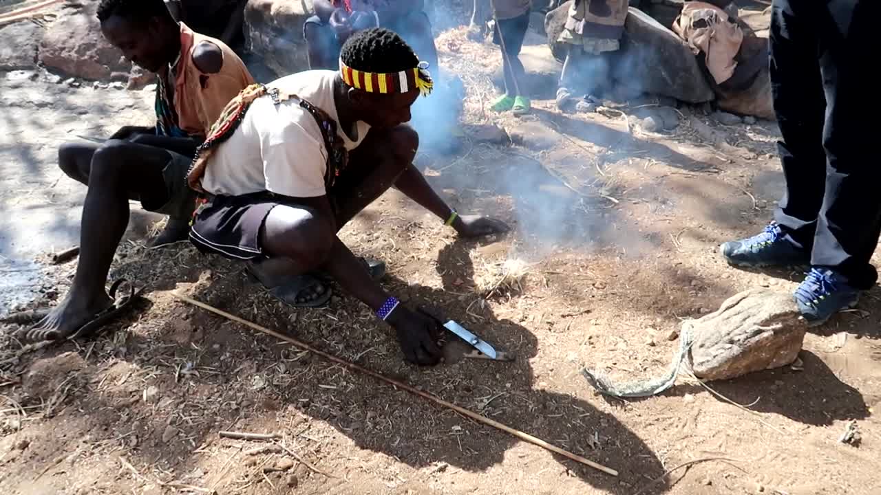 Tourists learning to make a fire with a Hadzabe tribe member in Tanzania, Africa