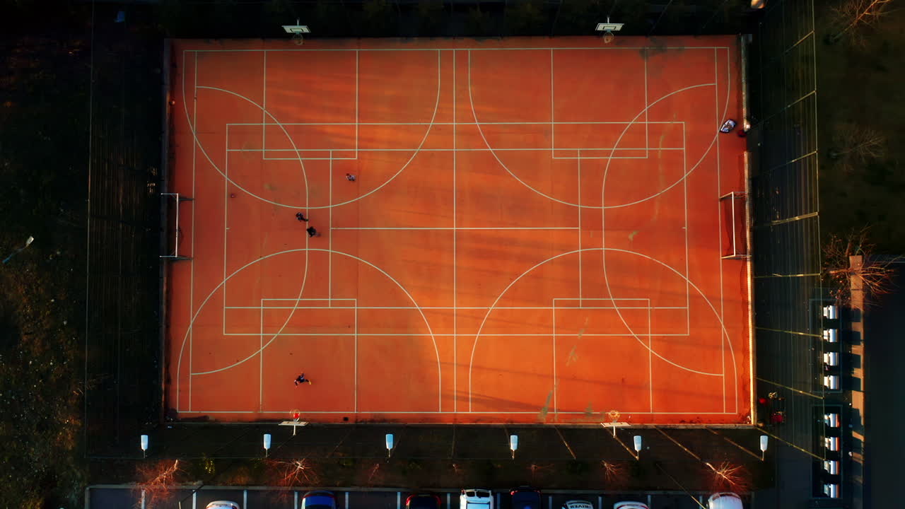 Vista aerea dall'alto di alcune persone che giocano a basket su un campo arancione al tramonto