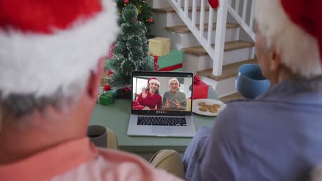 Happy-senior-caucasian-couple-on-video-call-on-laptop-with-senior-friends-at-christmas-time