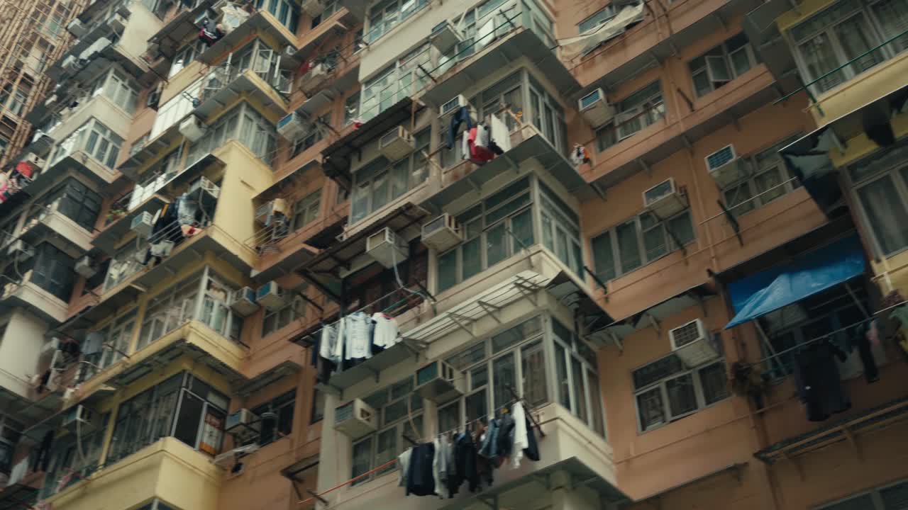 Inquadratura statica ravvicinata dal basso della facciata del densamente popolato Yick Cheong Building a Quarry Bay, Hong Kong, che mostra appartamenti sovrapposti con bucato steso, unità di condizionamento e balconi invecchiati.