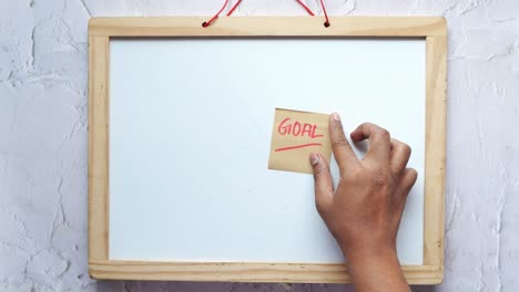 Kleben-Sie-Eine-Haftnotiz-Mit-Dem-Wort-„Ziel“-Auf-Eine-Weiße-Tafel