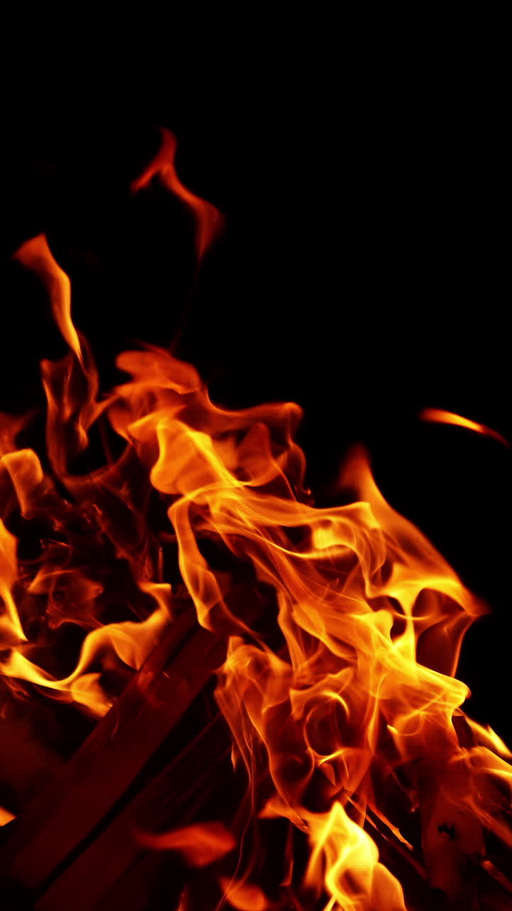 Pezzi di legno impilati bruciano nel falò. Falò acceso all'aperto di notte. Video verticale