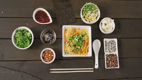 composition of bowls with pad thai, vegetables, sauces and spices on wooden background