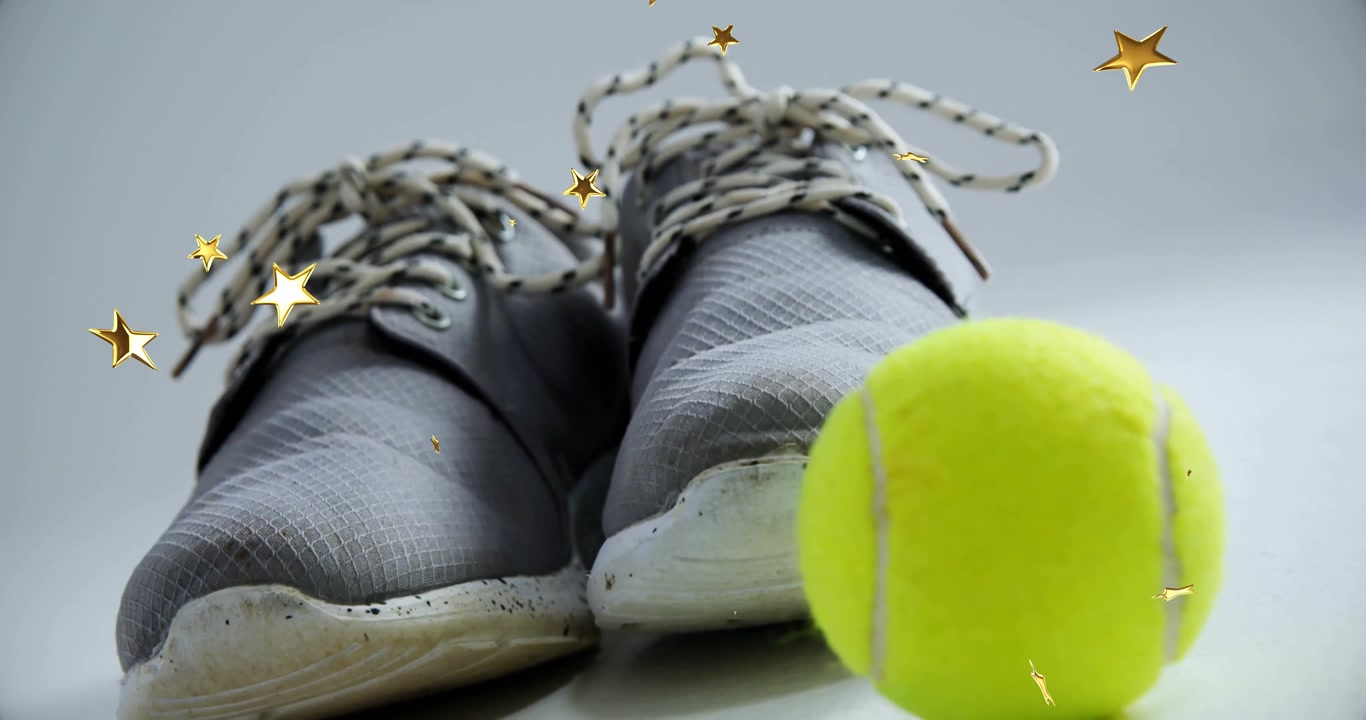 Tennis ball entering frame rolling beside sneakers while confetti drifting to showcase sports gear