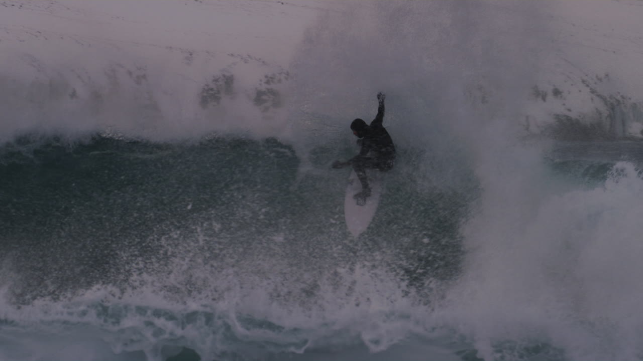 Surfer drops into large Arctic wave in Iceland, icy waters glisten under cloudy skies