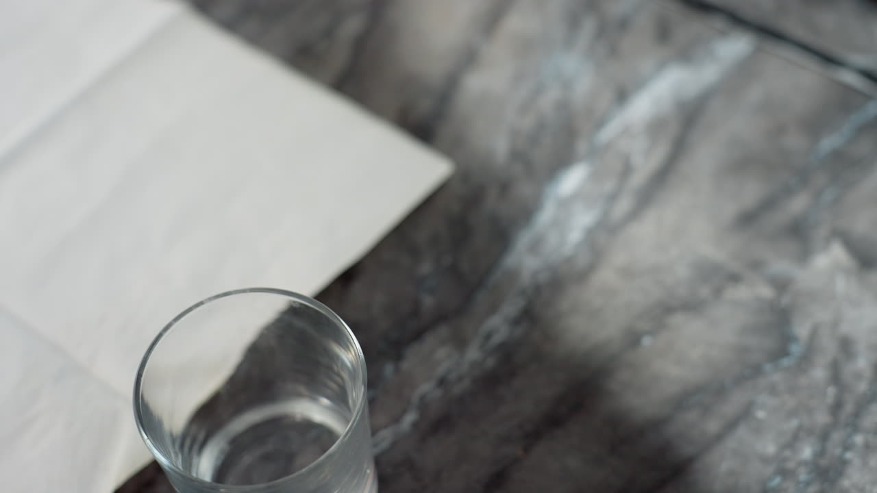 Close up of three clear glass cups arranged neatly on marble countertop near folded white paper napkin under soft lighting, creating serene domestic kitchen scene with elegant minimalistic detail