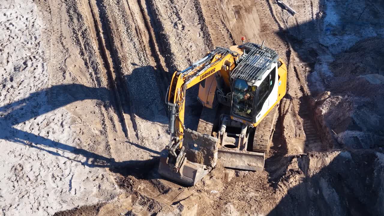 Excavator moves and loads dirt at sunny construction site, captured by drone in Gold Coast