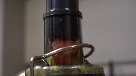 close-up fruits in juicer and person pressing fruits into electric juicer - male caucasian hand pushing fruits down into electric juicer home kitchen appliance to make healthy fresh fruit juice