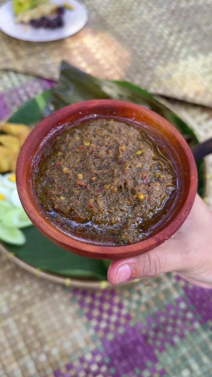 Käsi pitelee pientä puista kulhoa mausteista sambal-kastiketta