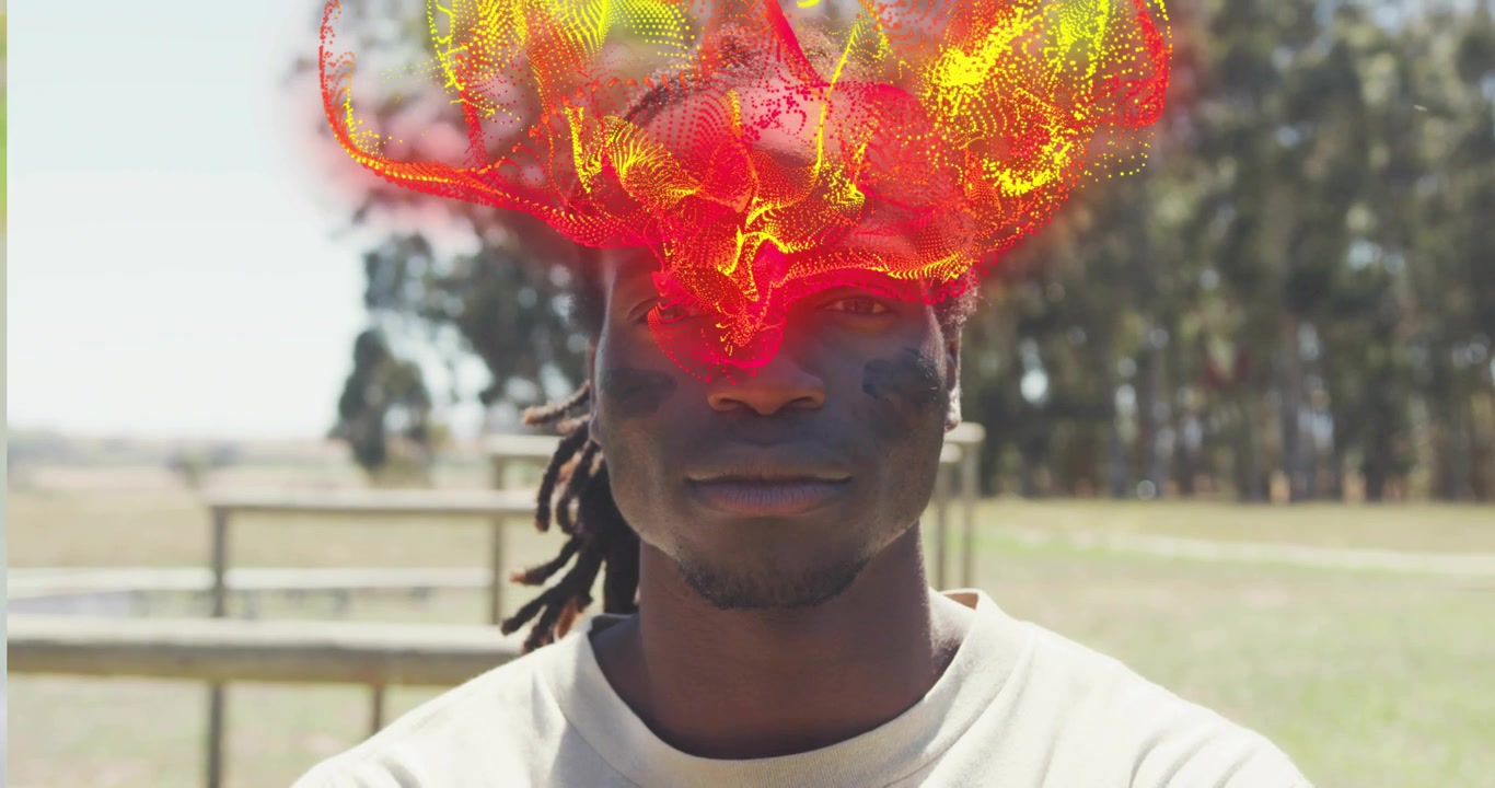 Man standing in field with tech particles appearing above head, swirling and forming energy mask