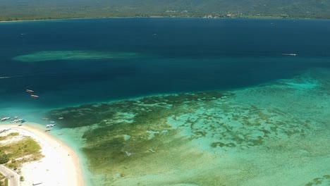 Beautiful-drone-shot-located-off-the-coast-of-the-Gili-islands-with-mountains-in-the-horizon-and-coral-reefs-surrounding-the-island-in-Indonesia