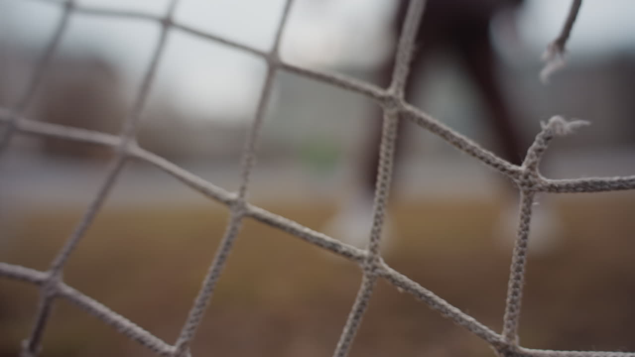 silueta naznačující bezprostřední akci, scéna městských sportů s překážkou a pohybující se siluetou, síť v popředí a bariéra vytvářejí napjatou atmosféru s blížícím se hráčem v městském prostředí