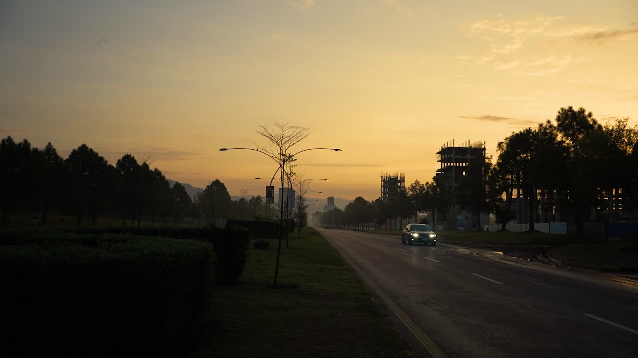 A beautiful cinematic morning view of Islamabad with a yellowish sky with sunrise and buildings under construction on Margalla Road while cars are passing by