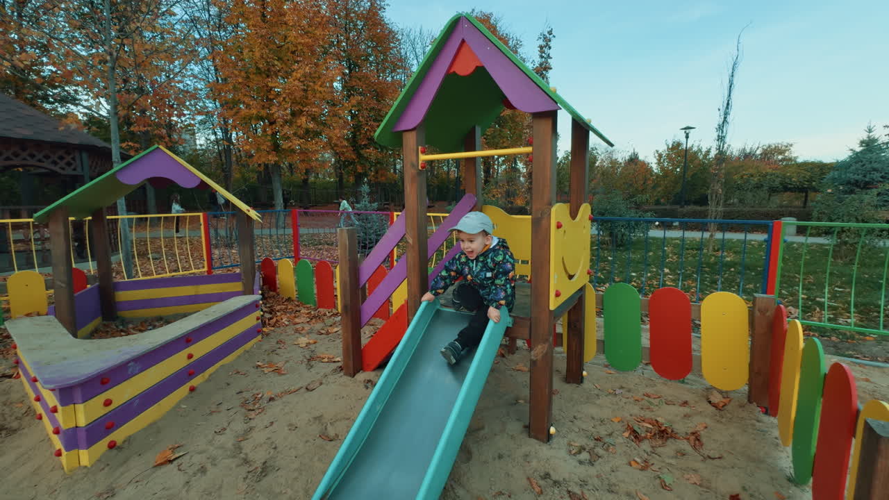 Happy smiling kid sits on the slide tapping his feet. Energetic cheerful child on the playground.
