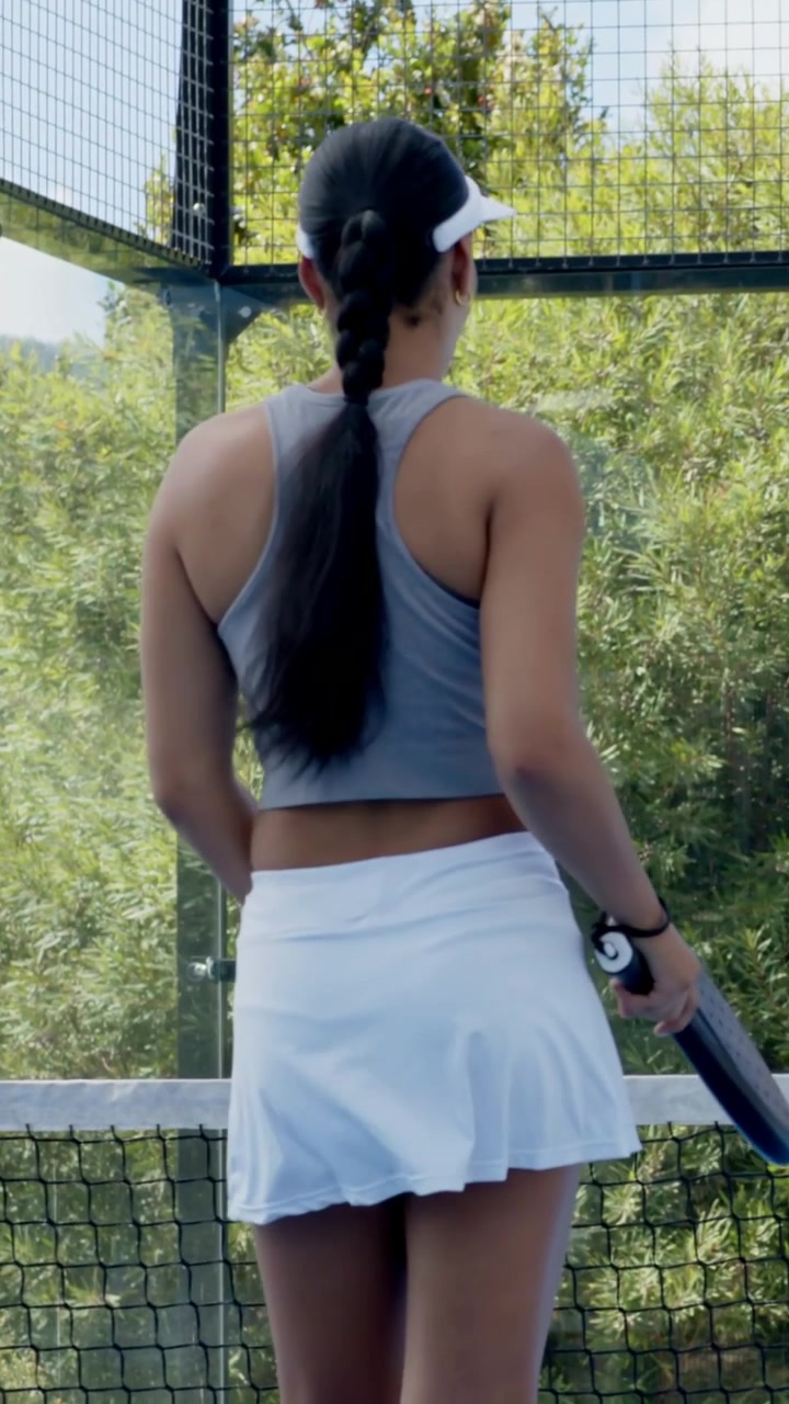 Vertical video: Walking woman holding paddle in tank skirt at net spotting ball, bending, picking