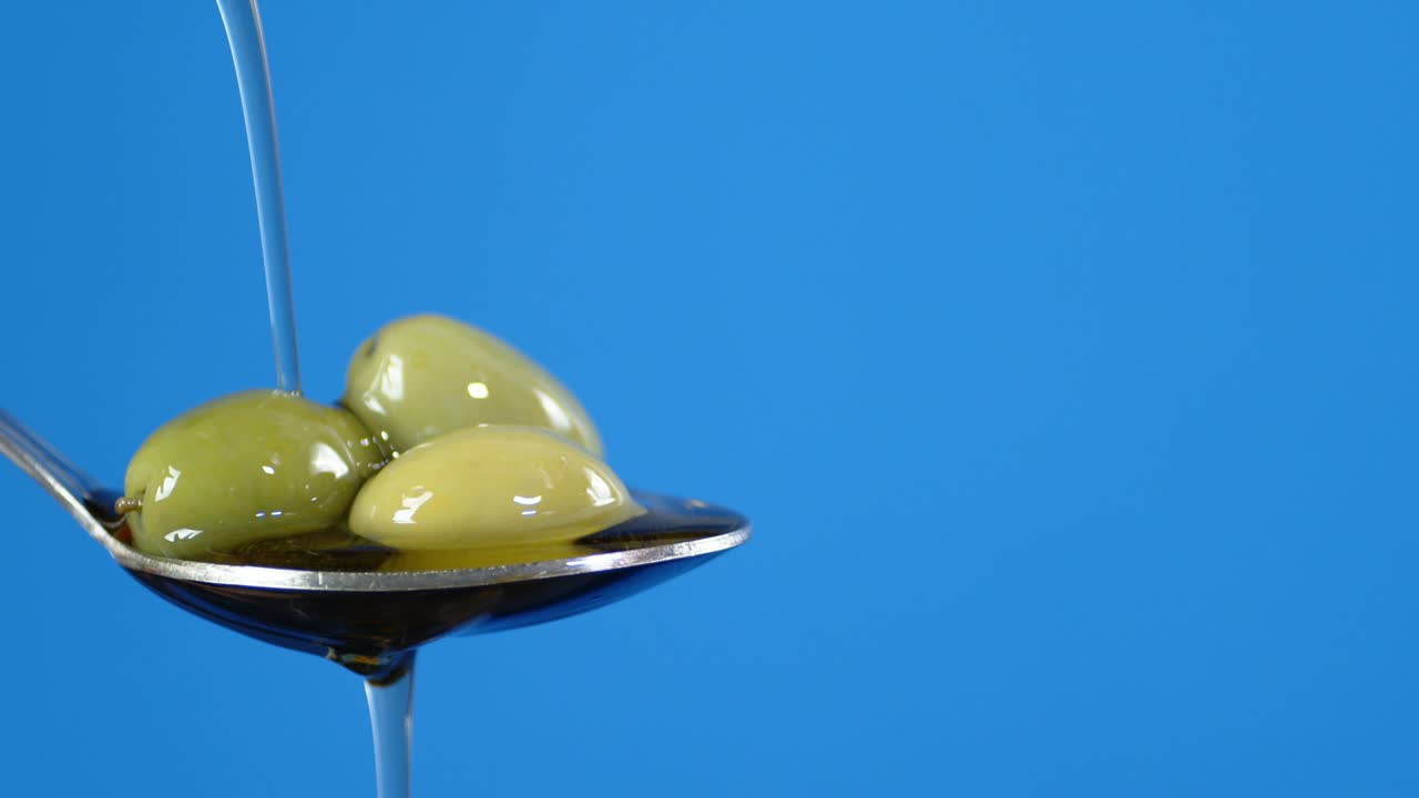 On a spoon with olives pouring olive oil.