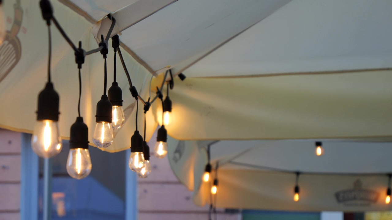 Rows of warm hanging bulbs decorate a restaurant exterior on a historic town street during the evening