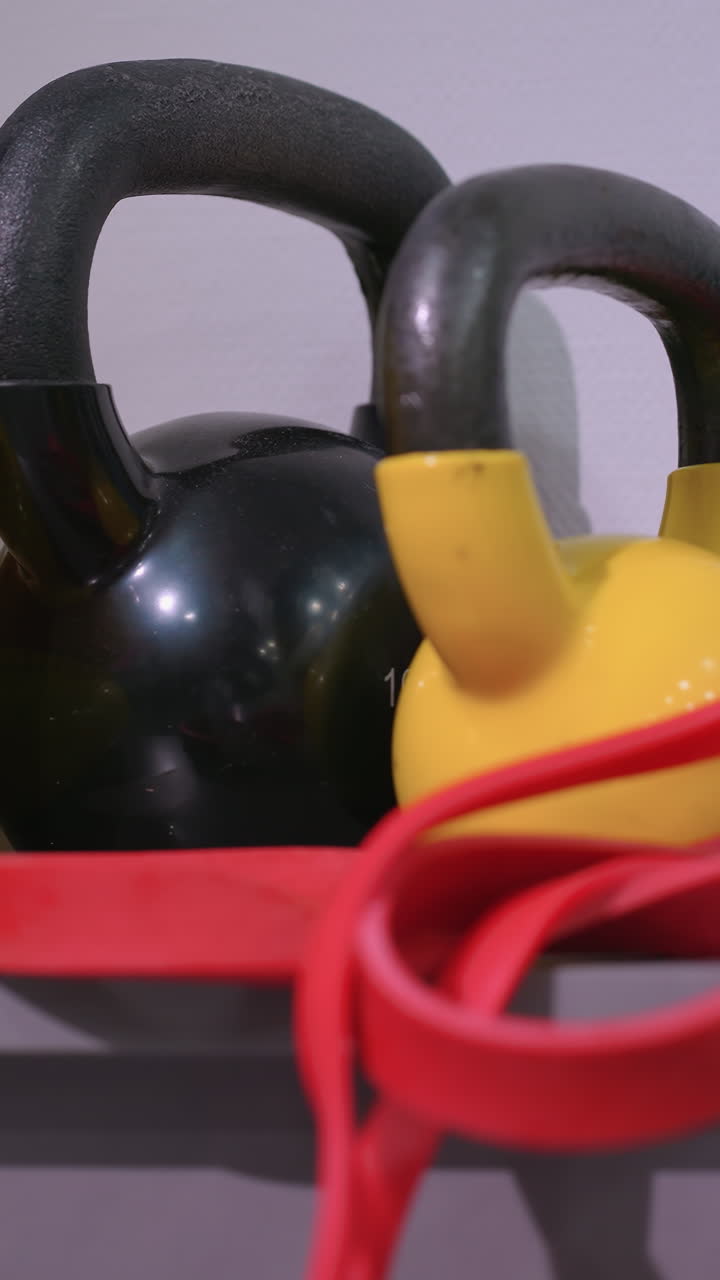 primer plano de varios equipos de gimnasia, incluidas kettlebells, bandas de resistencia y discos de equilibrio, ordenadamente dispuestos en un estante para entrenamiento de fuerza, ejercicios funcionales