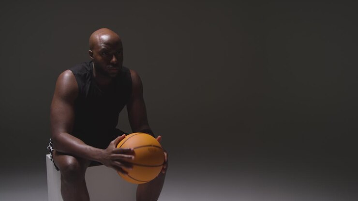 Studioaufnahme von sitzendem männlichem Basketballspieler mit Ball in den Händen 1