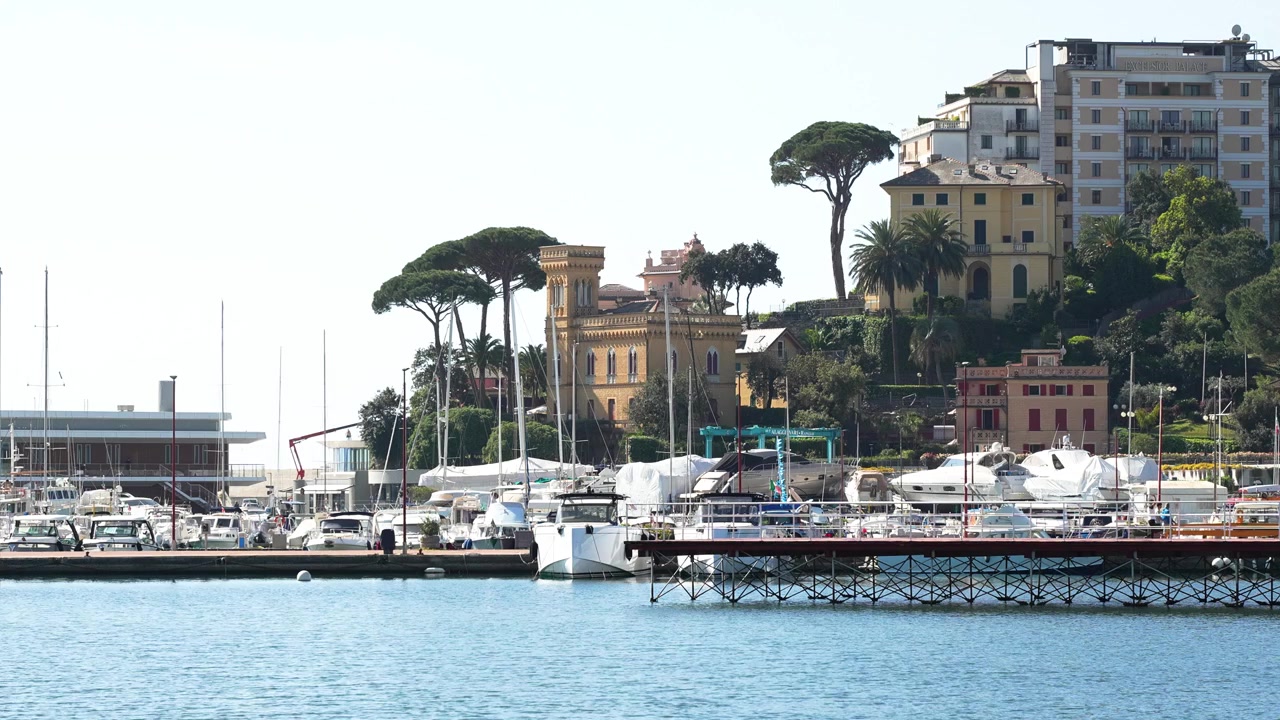 Ampia inquadratura statica e luminosa del porto turistico di Rapallo in Italia, con yacht di lusso, eleganti pini mediterranei, ville storiche ed edifici sul lungomare in una giornata di sole. Acqua cristallina